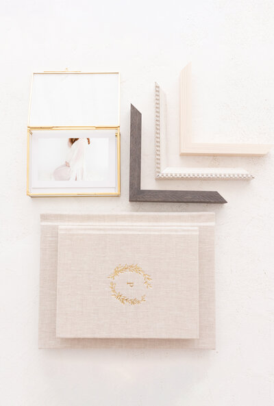 A stack of linen albums next to frame corners and a glass box with printed photos