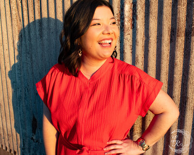 Photo of Ashlyn in a red dress, left hand on hip and looking over her left shoulder while laughing