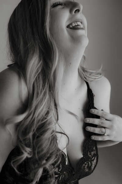 Black and white photo of woman in black lingerie leaning her head back and laughing