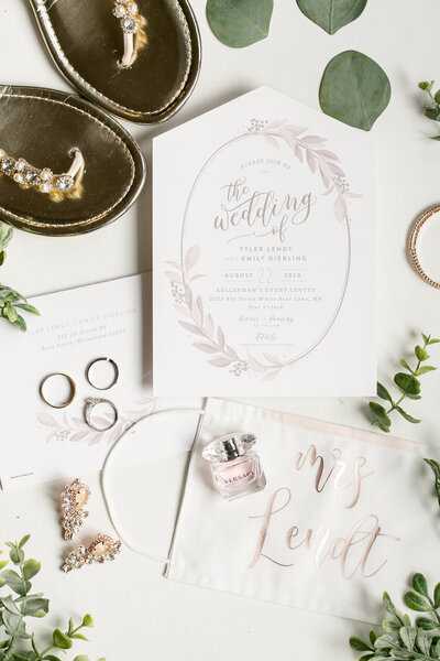 Wedding day details with the invitation, sandals, rings, and greenery