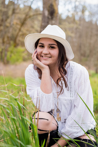 High school senior girl posing in green grass with tress in the background for senior photos