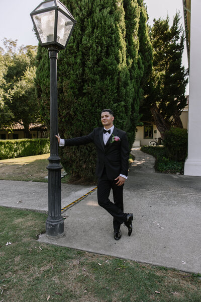 The groom is leaning on a lamp post.
