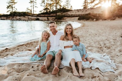 A family of four in beachy colors sitting in the sand at Tahoe Beach.
