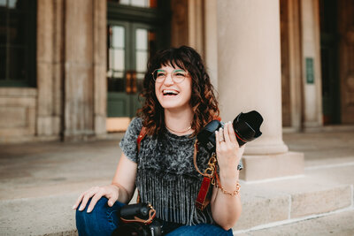 A woman smiles while holding a camera