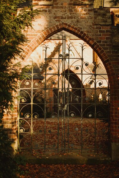 Old iron gate framed by brick archway surrounded by autumn leaves, representing the gateway to transformation and self-discovery.