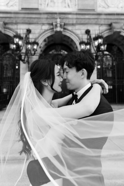 Rhode Island Wedding Photographers | Kelsey Sheehan Photography Timeless Rhode Island Weddings | A joyful couple embraces on their wedding day, with the bride's veil flowing. They're in front of an ornate building, exuding love and happiness.