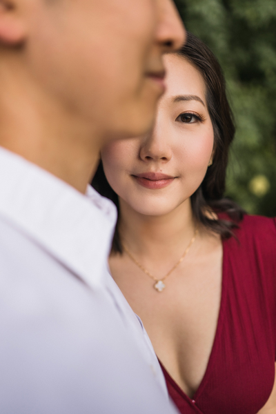 Groom kisses the smiling bride's cheek amidst a field of wildflowers during a romantic outdoor engagement session. Bride's natural makeup and elegant hair by Kohnur.
