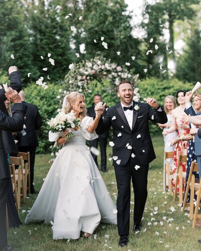 A wedding portrait of a bride and groom walking down the aisle at their wedding ceremony after saying "I do" with flower petals in the air at Little River Farms.