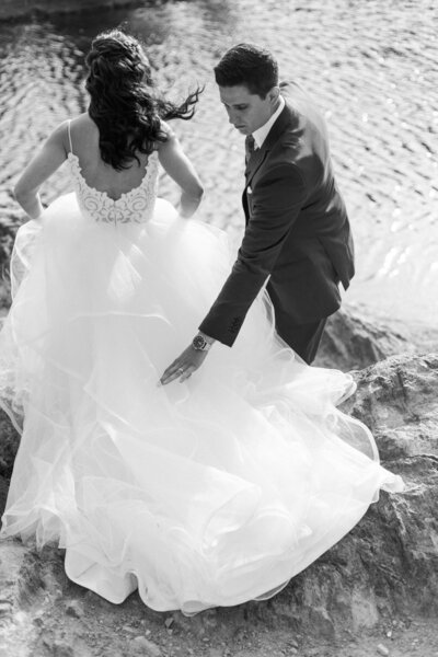 black and white photo of dress blowing in wind with bride and groom