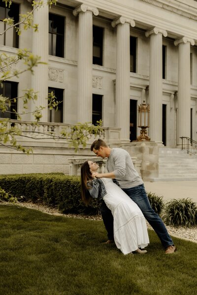 An engaged couple performs a dip in front of an elegant downtown building in Cedar Rapids Iowa.