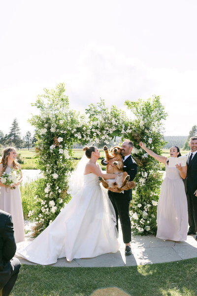 Bride and groom holding their dog during their outdoor wedding ceremony.