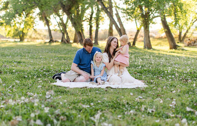 family sitting on a blanket in a field and snuggling during family photos