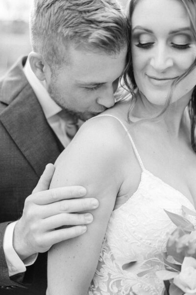 black and white portrait of bride and groom kissing on shoulder
