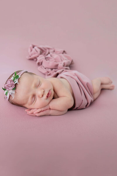 newborn baby girl wrapped in pink laying on her side for her Burlington, Ontario newborn photography session in Burlington, Ontario.