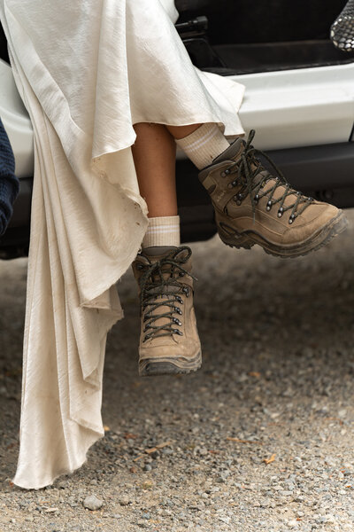 Close up of someone's feet wearing hiking boots with a wedding dress draped over them.
