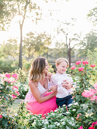 An expecting mother holding her son in a rose garden.