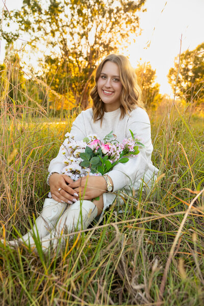 Senior photo session of Abby sitting in a field at the Arboretum with flowers in her boots in Lawrence KS | Senior Photographer in Lawrence KS