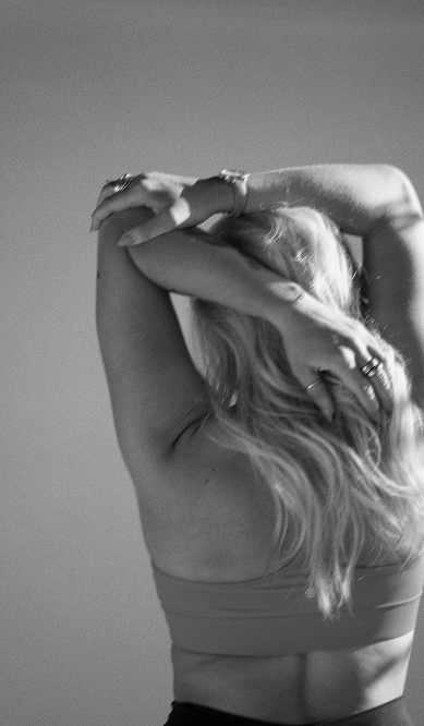 Black and white image of Kaylin's back as she is stretching with arm overhead 
