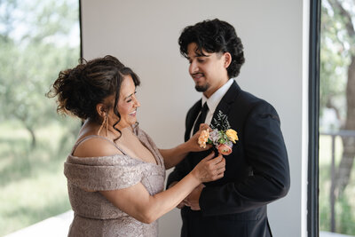 mother of the groom puts flowers on son's suit on wedding day
