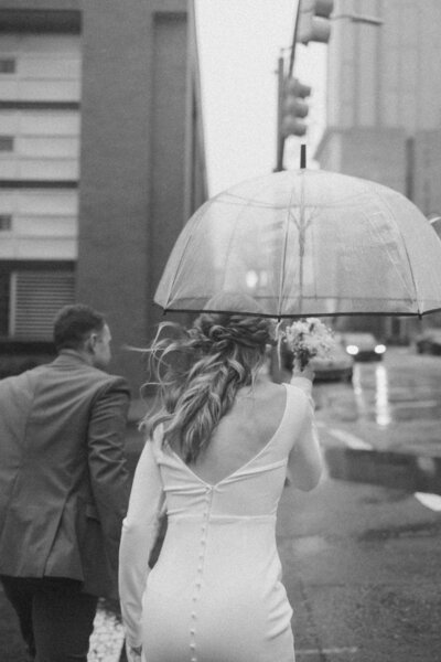 The bride and groom joyfully run through the rainy city streets, hand in hand.