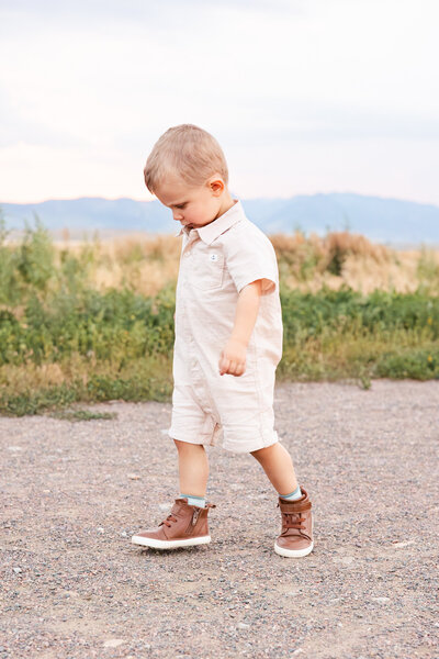 A little boy in a white jumpsuit walks on a path.