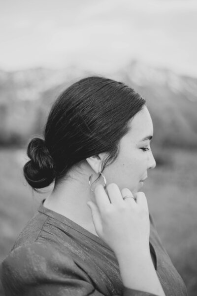 Girl in red dress sitting on a ledge and looking back over her shoulder with a pretty mountain range viewed in the background