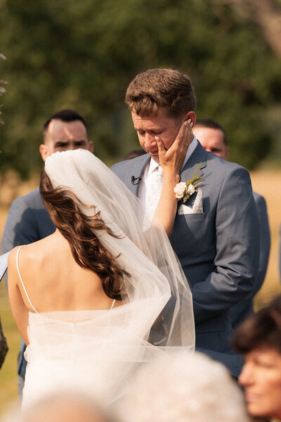 a bride wiping tears off a groom's face during their emotional wedding ceremony