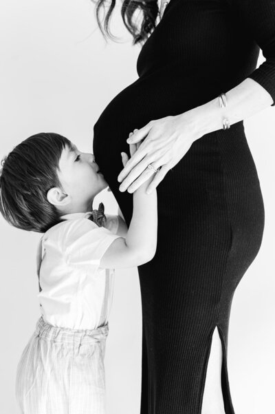 A little boy looks up  kissing  his moms pregnant belly by Casey McMurray Photography