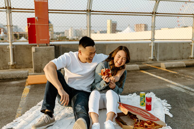 J & J laughing & sitting on a rooftop while eating pizza