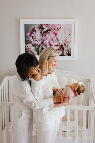 Two moms hold and look at their new baby girl in her nursery.
