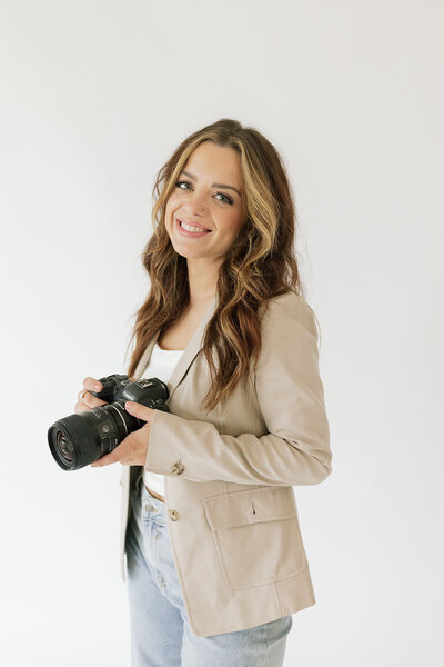 Headshot of photographer  Charity White , posing in a seated position, smiling, and holding a camera