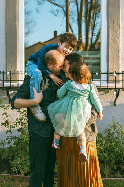 boy sitting on dad's shoulders while dad and mom nuzzle noses and mom holds baby daughter