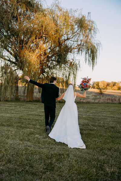 Wedding couple portraits of couple walking away cheering under a willow tree