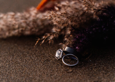 A couples wedding rings for their Oregon coast elopement rest on a sandy beach.