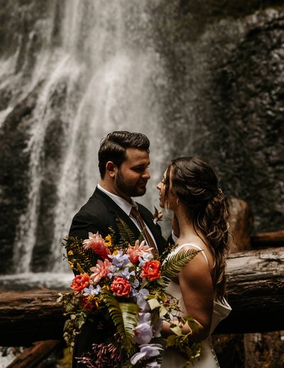 man and woman standing close together to exchange their vows on their wedding day at a waterfall elopement in the rainforest of vancouver island