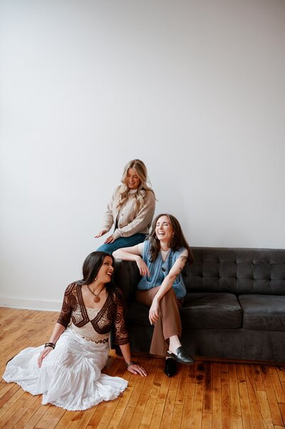 The Content by Liz team perched on a couch and smiling and laughing.