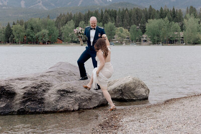 Groom helping bride step up onto a rock in the water in White Fish Montanta