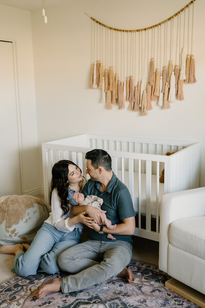 new parents sit with newborn in front of crib