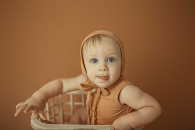 young kid celebrating  his birthday  with  milestone photoshoot. The baby is wearing a light brown onesie and a matching cap.