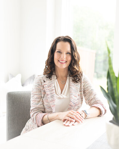 branding headshot portrait woman in light tweed blazer at light table with plant behind her