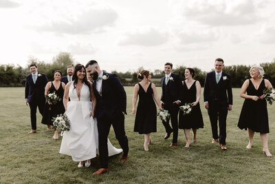 bride and groom with wedding party walking in a field and laughing