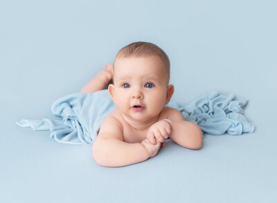 Brooklyn, NY Photographer captures twin baby boy and girl for baby milestone portrait. Babies are sitting beside each other on an infant daybed. Baby girl is in a white organza ruffled onesie and baby boy is in a taupe knit romper and bonnet.