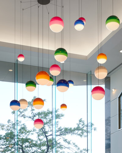 A cluster of tritone globe pendant lights hanging from the ceiling in front of a bright window