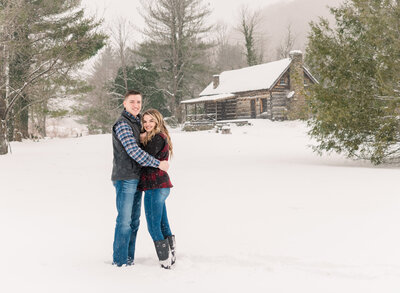 engaged couple hugging and looking at the camera in the snow