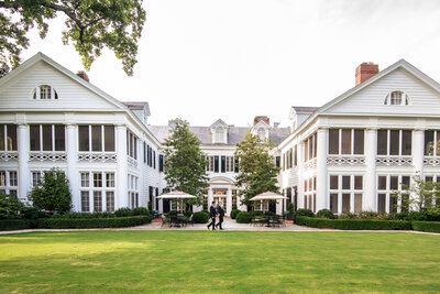 LGBTQ-elopement-couple-walking-across-the-back-lawn-of-The-Duke-Mansion-showcasing-the-hotel-in-Charlotte-NC