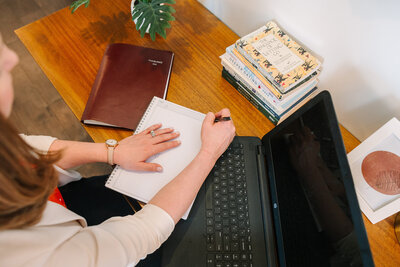 Lindsay writing in a notebook next to her laptop