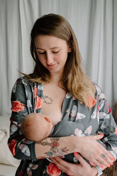 Newborn photo of mom in floral robe with newborn daughter in matching blanket in studio.