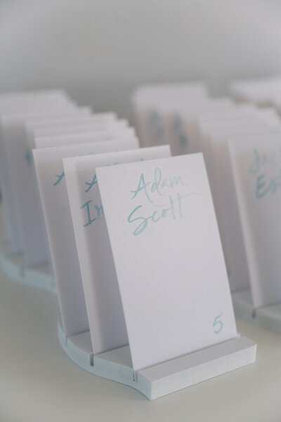 White  escort card display with blue  watercolor lettering for Connecticut shoreline  wedding
