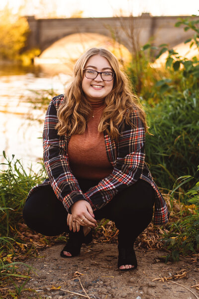 Young woman posing in front of the river with beautiful fall colors in the background.