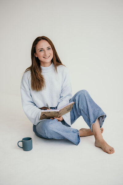 Woman is sitting comfortably on the ground while writing into a notebook.
